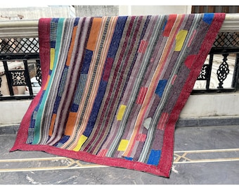 Puede incluir: Una colcha de retazos colorida con un borde rojo. La colcha está hecha de varias telas en tonos de azul, verde, naranja, amarillo y rojo. La colcha está doblada y drapeada sobre una barandilla.