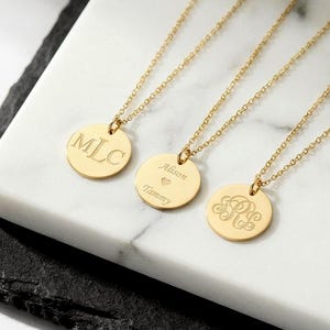 May include: Gold-coloured pendant necklaces with personalised engravings. The pendants are round and hang from delicate chains. One pendant has the initials "MLC", another has the names "Alison" and "Tammy" with a heart, and the third has the initials "R&E".