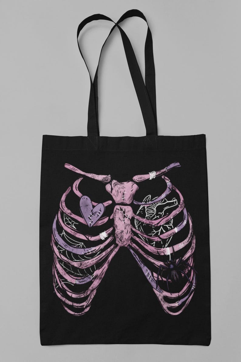 Puede incluir: Bolso tote negro con un dise&ntilde;o de caja tor&aacute;cica rosa y morado. La caja tor&aacute;cica tiene un coraz&oacute;n con un dise&ntilde;o cosido y una ara&ntilde;a. El bolso tiene dos asas negras.
