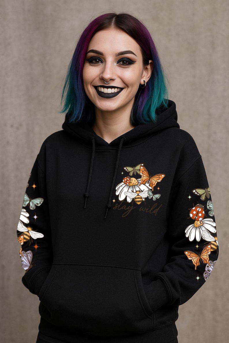 May include: Black hoodie with a floral and insect design. The design includes butterflies, daisies, and bees, with the words "stay wild" in script. The sleeves also feature the same design. The hoodie has a drawstring hood and a front pocket.