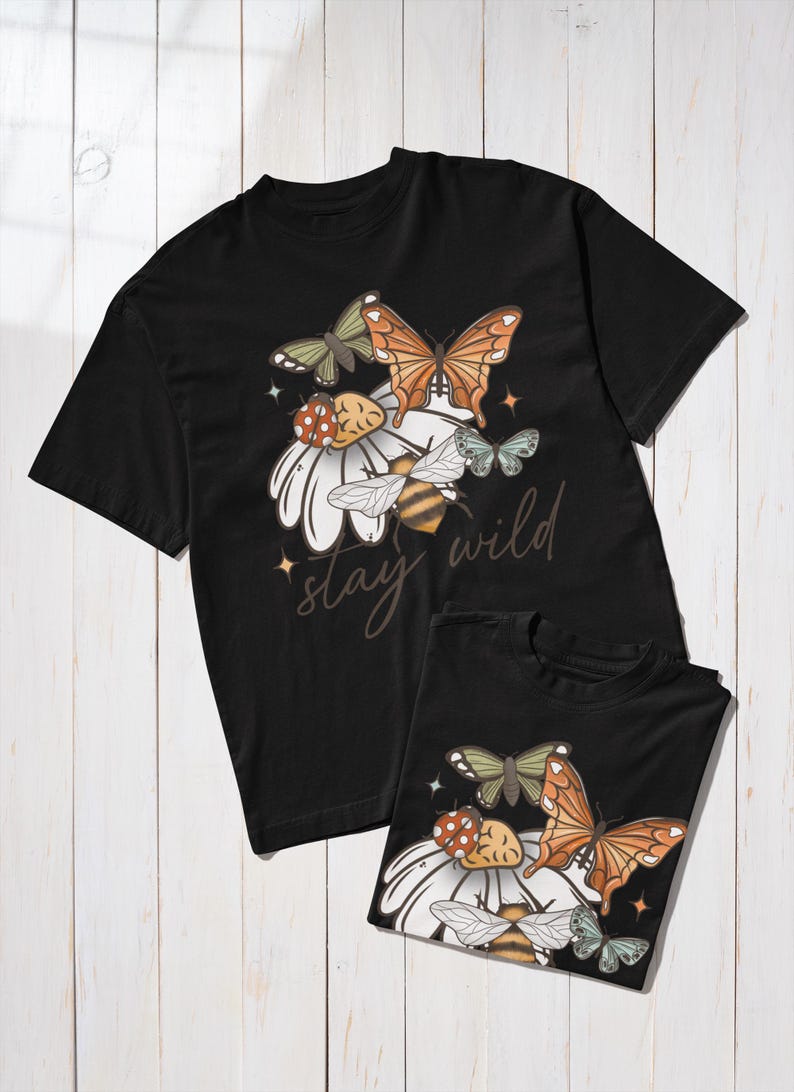 May include: Black t-shirts with a floral and insect design. The design includes butterflies, a bee, and a ladybug on a white daisy. The text "stay wild" is written in a script font.