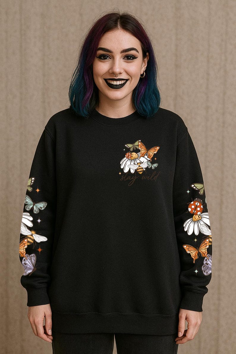 May include: Black sweatshirt with a floral and butterfly design. The design includes daisies, butterflies, and a bee, with the words "stay wild" in script. The sleeves also feature the same design. The sweatshirt is a crew neck.