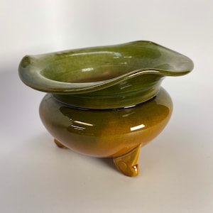May include: A green and brown ceramic planter with a wide, flared rim and three short legs.