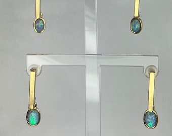 May include: A pair of gold earrings with oval-shaped opal stones. The earrings are hanging from a gold bar.
