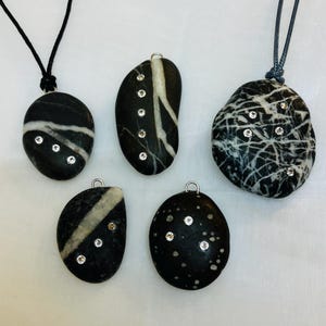 Peut inclure: Cinq pendentifs en pierre noire et blanche avec des accents argentés et de petites pierres précieuses claires. Chaque pendentif a un motif unique de lignes blanches sur un fond noir.
