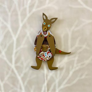 May include: A brown wooden kangaroo puppet with a patterned fabric body and blue eyes. The kangaroo is holding a smaller kangaroo puppet in its pouch.