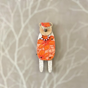 May include: Orange and white fabric doll with a white face, black eyes, and a black nose. The doll is wearing a white necklace with black beads and a white hat.