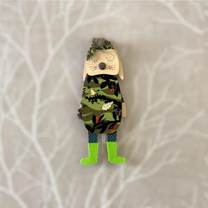 May include: A wooden toy animal with a camouflage pattern and green boots. The toy has a brown nose, black eyes, and a white headband.
