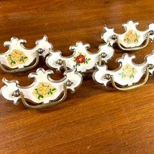 Op de afbeelding: Vijf antieke witte porseleinen kastladegrepen met bloemmotieven en messing beslag.