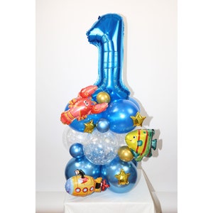 Könnte beinhalten: Ein blauer Ballon in Form der Zahl Eins mit Dekorationen aus Ballon-Hummer, -Fisch und -U-Boot. Die Ballons sind in Form eines Turms angeordnet.
