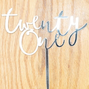 May include: Silver glitter cake topper with the words "twenty one" in a cursive script.