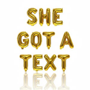 Può includere: Palloncini a forma di lettere dorate che compongono la scritta "SHE GOT A TEXT" su sfondo bianco. I palloncini sono gonfiati e si riflettono sulla superficie sottostante. Ideale per una festa o una celebrazione.
