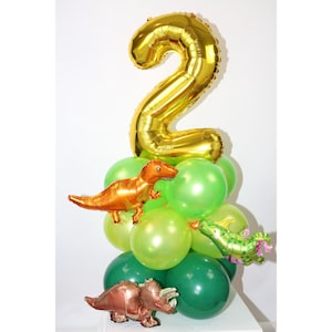 May include: A gold number two balloon with green and orange dinosaur balloons. The balloons are arranged in a tower shape.