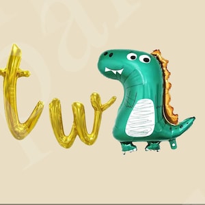 May include: Gold foil letter balloons spelling "two" with a green dinosaur balloon with orange spikes and white eyes.