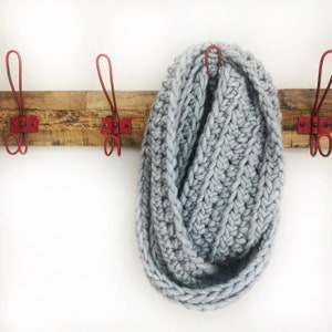 May include: A gray knitted infinity scarf hanging on a wooden rack with red metal hooks.