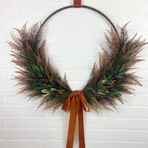 May include: A brown metal hoop wreath decorated with green and brown foliage and a burnt orange velvet ribbon.