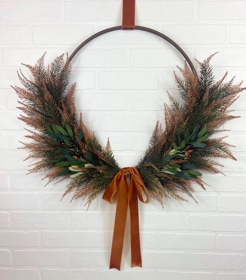 May include: A brown metal hoop wreath decorated with green and brown foliage and a burnt orange velvet ribbon.