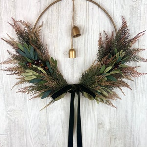 May include: A gold metal wreath with green and brown foliage and a black velvet ribbon. Two gold bells hang from the wreath.