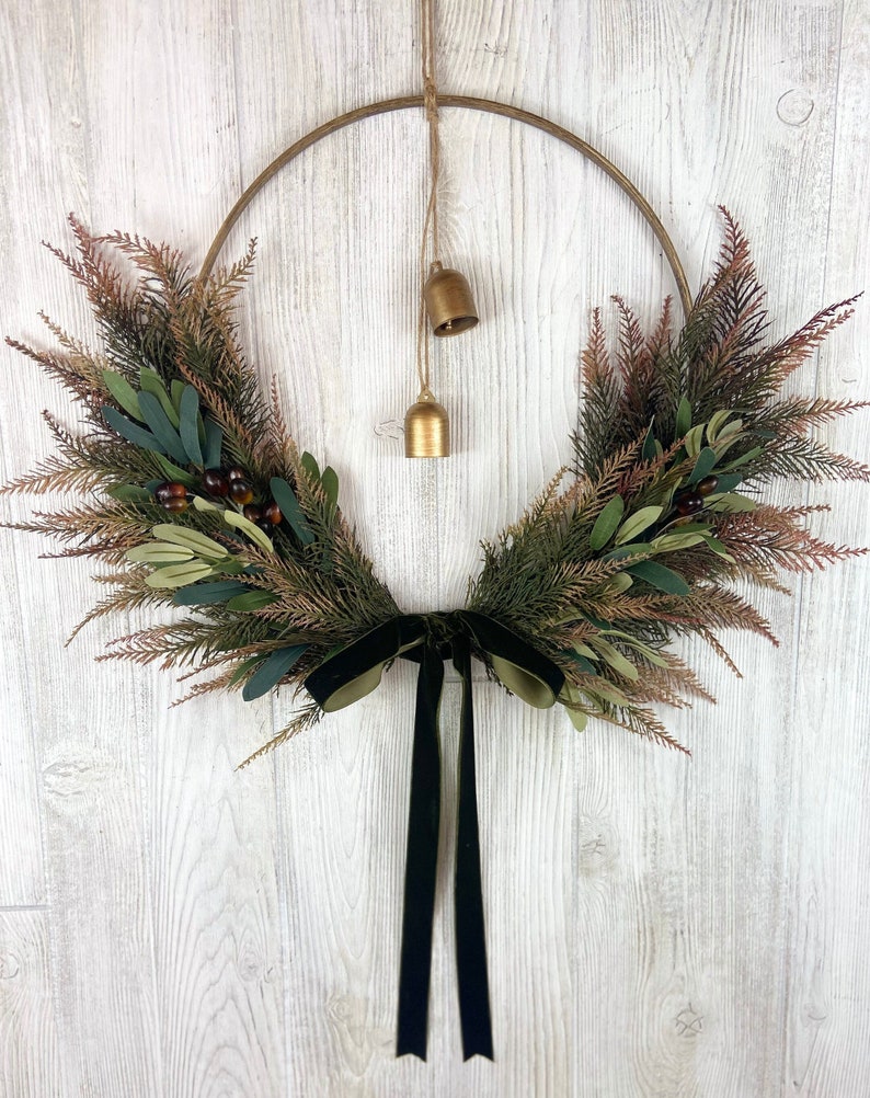 May include: A gold metal wreath with green and brown foliage and a black velvet ribbon. The wreath has two small gold bells hanging from it.