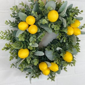 May include: A green and gray wreath with yellow lemons. The wreath is made of eucalyptus and lambs ear.