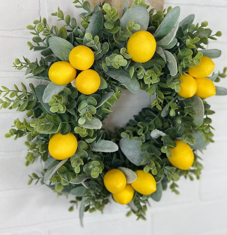 May include: A green and gray wreath with yellow lemons. The wreath is made of eucalyptus and lambs ear.