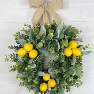 May include: A green and gray wreath with yellow lemons and a brown bow with white polka dots.