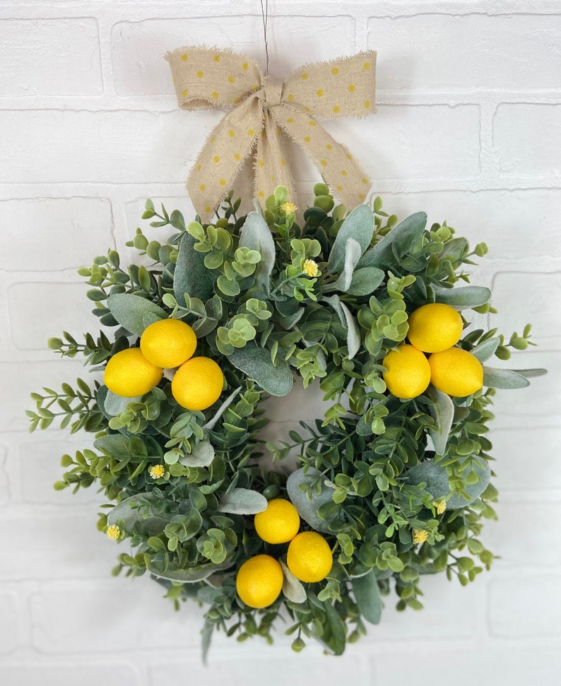 May include: A green and gray wreath with yellow lemons and a brown bow with white polka dots.