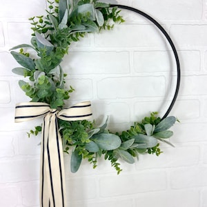 May include: A black metal wreath with a green and gray eucalyptus garland and a black and white striped ribbon.