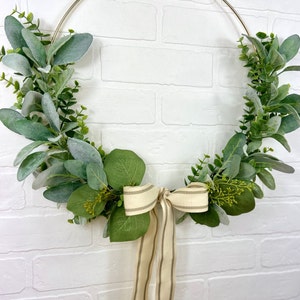 May include: A gold metal wreath with green eucalyptus leaves and a beige and brown striped ribbon bow.