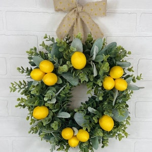 May include: A green and gray wreath with yellow lemons and a brown bow with white polka dots.