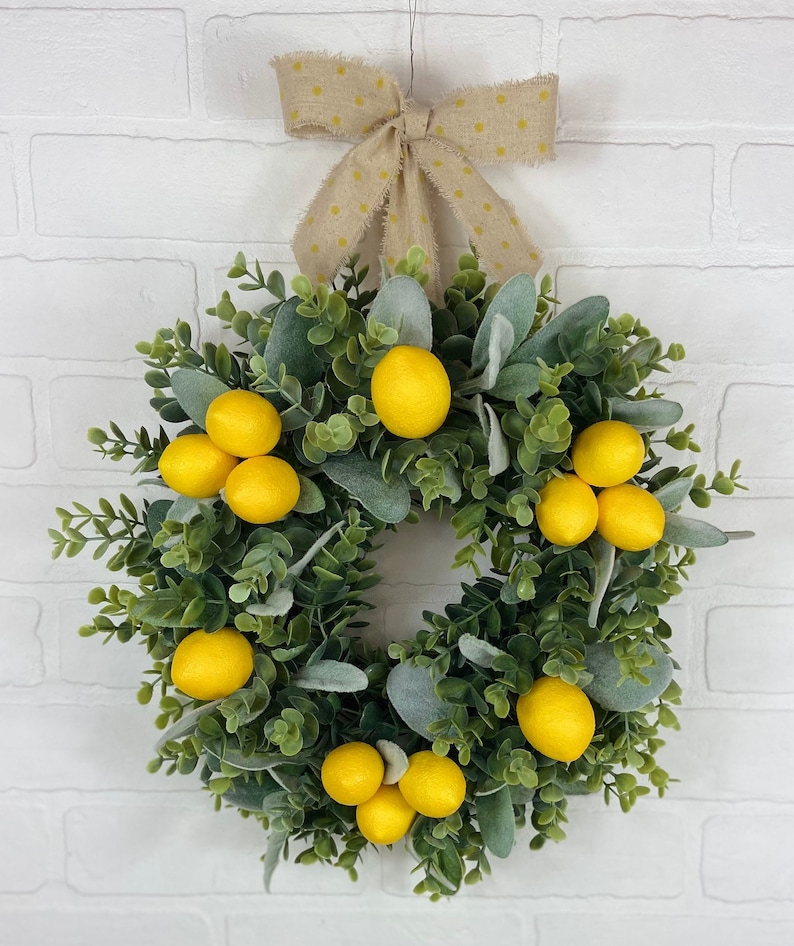 May include: A green and gray wreath with yellow lemons and a brown bow with white polka dots.