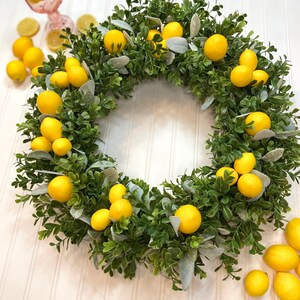 May include: A green boxwood wreath decorated with yellow lemons. The wreath is on a white background.