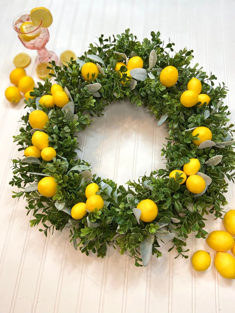 May include: A green boxwood wreath decorated with yellow lemons. The wreath is on a white background.