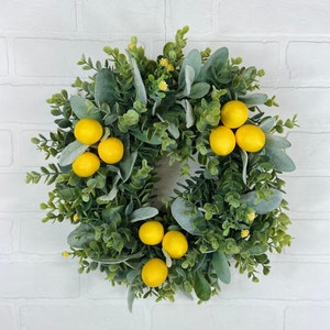 May include: A green wreath with faux lemons and eucalyptus leaves. The wreath is perfect for a spring or summer decor.