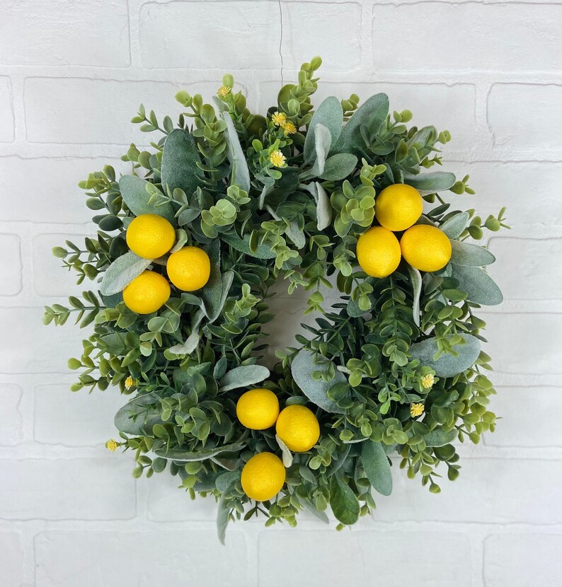May include: A green wreath with faux lemons and eucalyptus leaves. The wreath is perfect for a spring or summer decor.