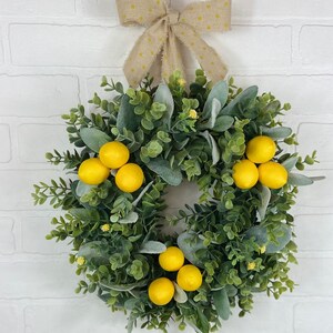 May include: A green and gray wreath with yellow lemons and a brown bow with white polka dots.