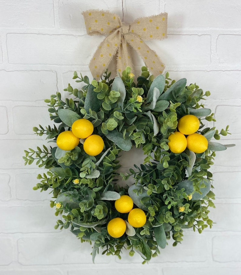 May include: A green and gray wreath with yellow lemons and a brown bow with white polka dots.
