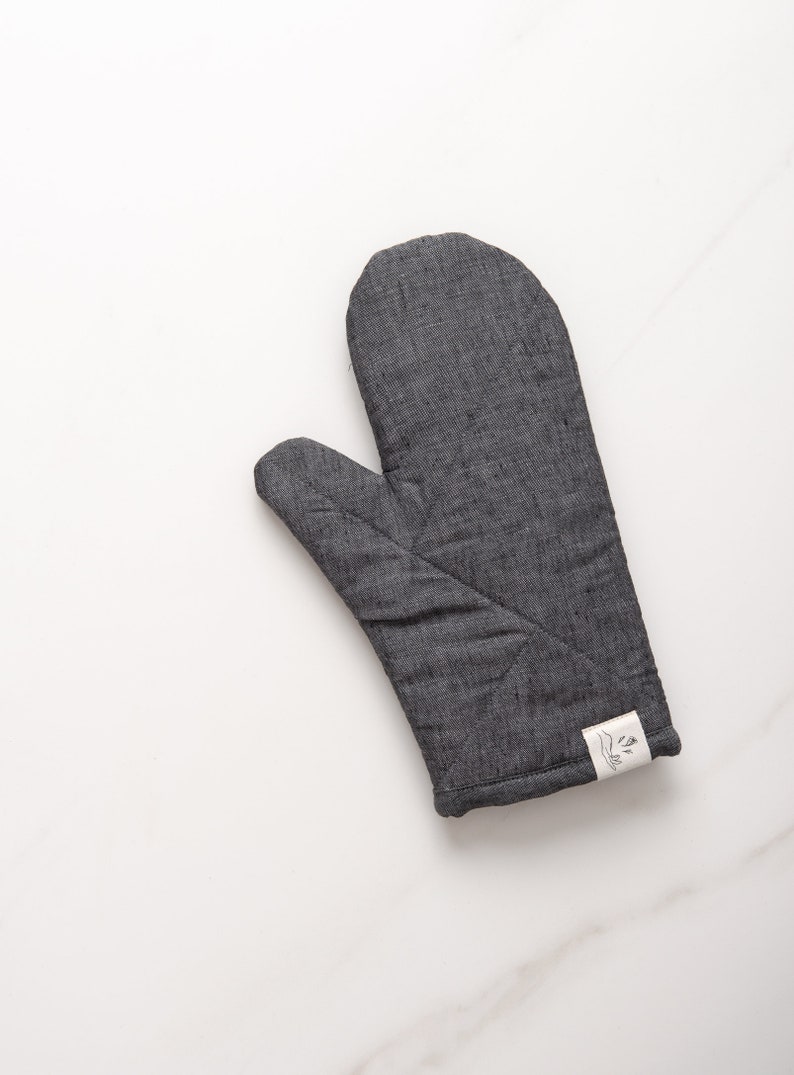 May include: A gray quilted oven mitt with a white label that says "The Little Market".