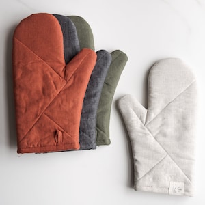 Può includere: Quattro guanti da forno in diversi colori: ruggine, grigio, verde e beige. I guanti sono realizzati in tessuto trapuntato e hanno un design semplice.