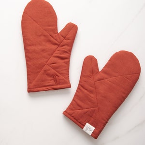 May include: A pair of rust-colored quilted oven mitts. The mitts are made of a thick, durable fabric and have a quilted design for added protection.