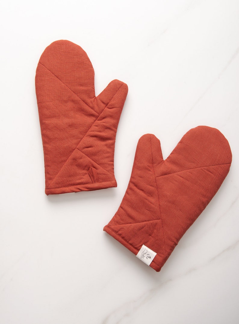 May include: A pair of rust-colored quilted oven mitts. The mitts are made of a thick, durable fabric and have a quilted design for added protection.