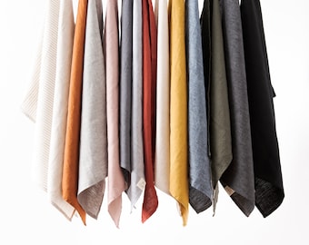 May include: A collection of 13 linen tea towels hanging on a wooden rod. The towels are in various colors, including white, gray, brown, orange, yellow, and black.