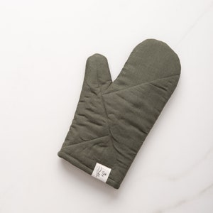 May include: A green quilted oven mitt with a white label that says "The Little Market".