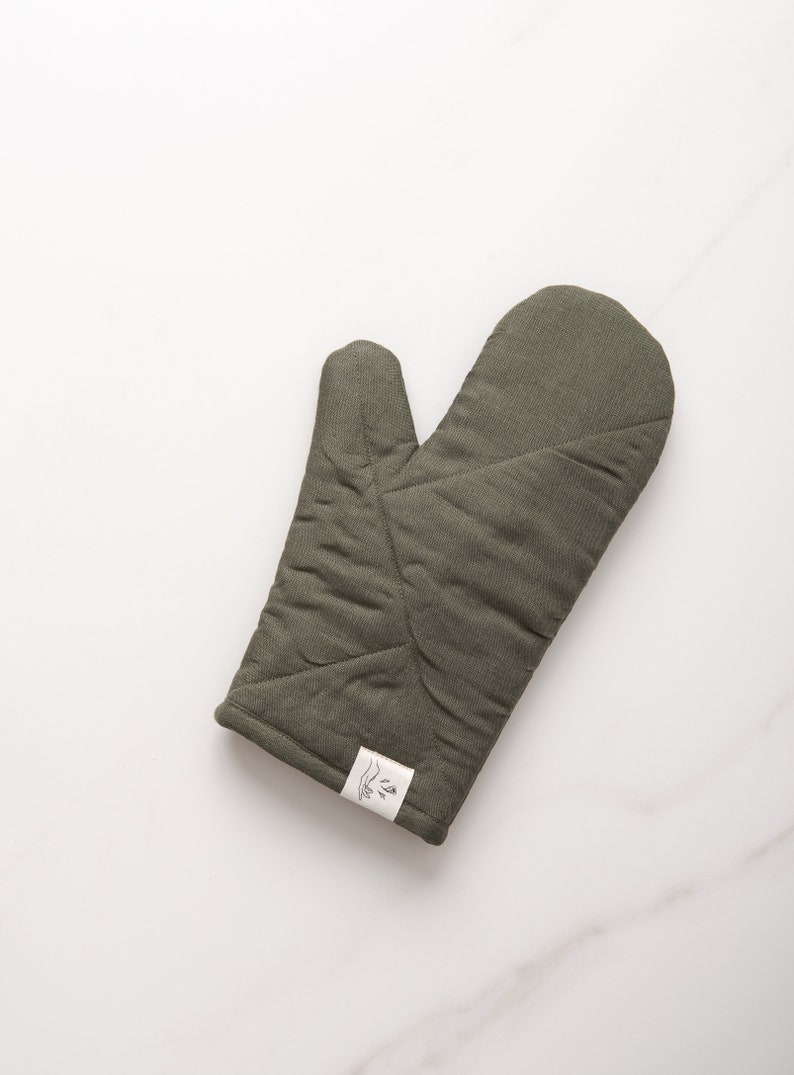 May include: A green quilted oven mitt with a white label that says "The Little Market".