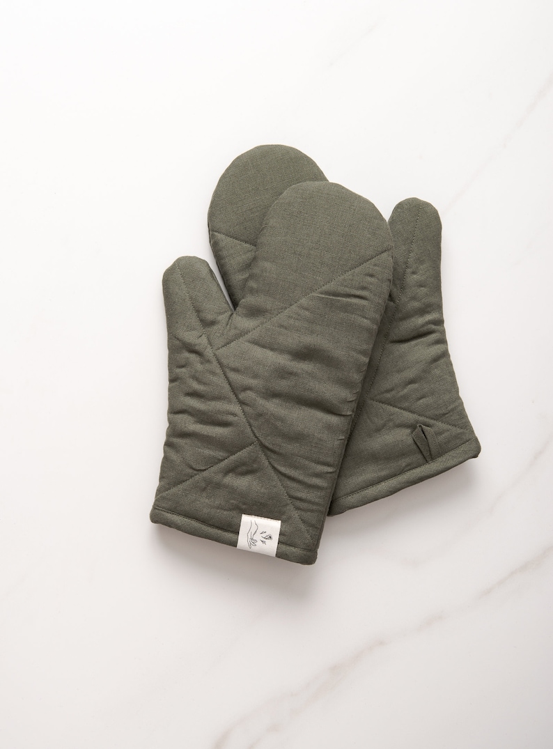May include: A pair of olive green quilted oven mitts with a white label that says "La Isla".