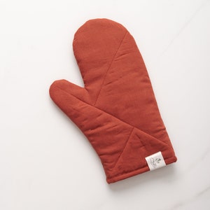May include: A rust-colored quilted oven mitt with a white label that says "Made with Love".