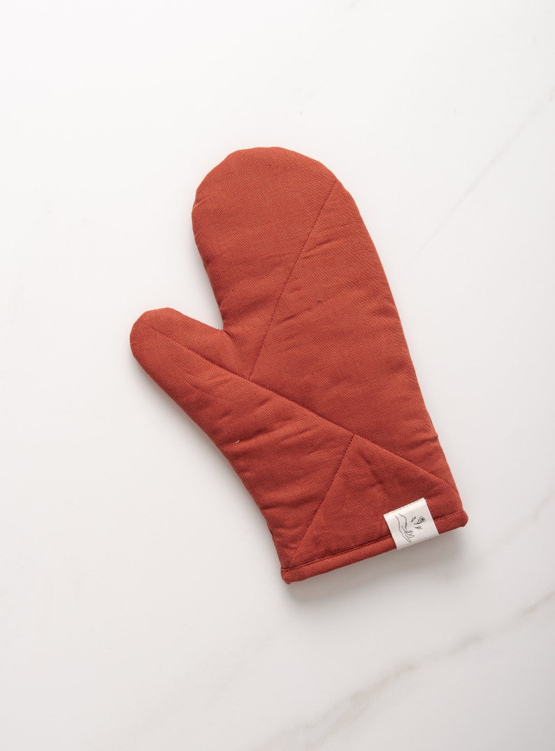 May include: A rust-colored quilted oven mitt with a white label that says "Made with Love".