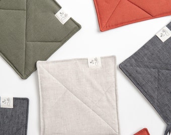 May include: Set of six quilted linen pot holders in various colors, including gray, green, beige, and red. Each pot holder has a small white label with a hand-drawn design.
