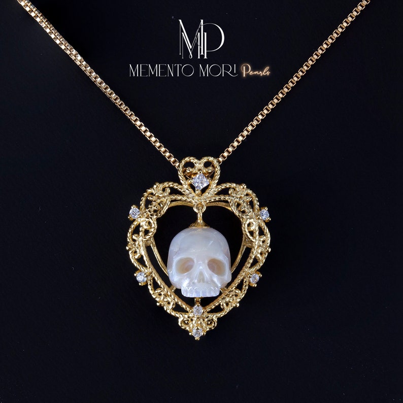May include: A gold heart-shaped pendant with a white pearl skull inside. The pendant is on a gold chain and has small diamonds around the edge.