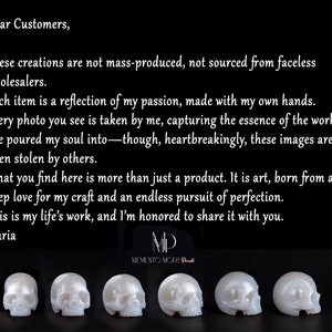 May include: Four white, hand-carved skull sculptures made of polished pearl. The sculptures are arranged in a row, with the skulls facing the viewer. The text "Memento Mori" is visible below the sculptures.